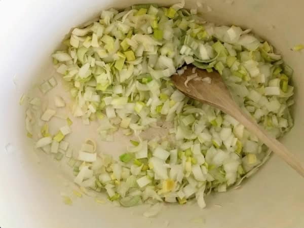 chopped onions and leek in Dutch oven stirring with wooden spoon