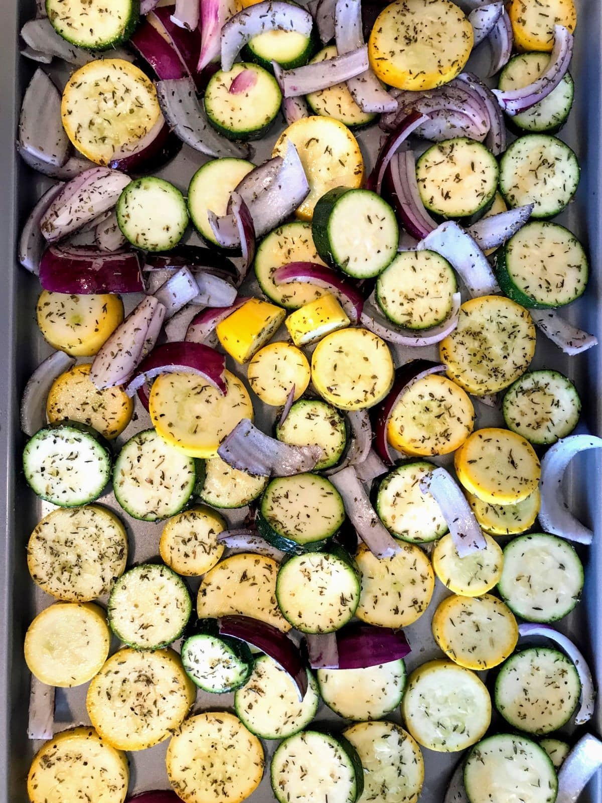 raw zucchini, yellow squash, and red onion on baking sheet