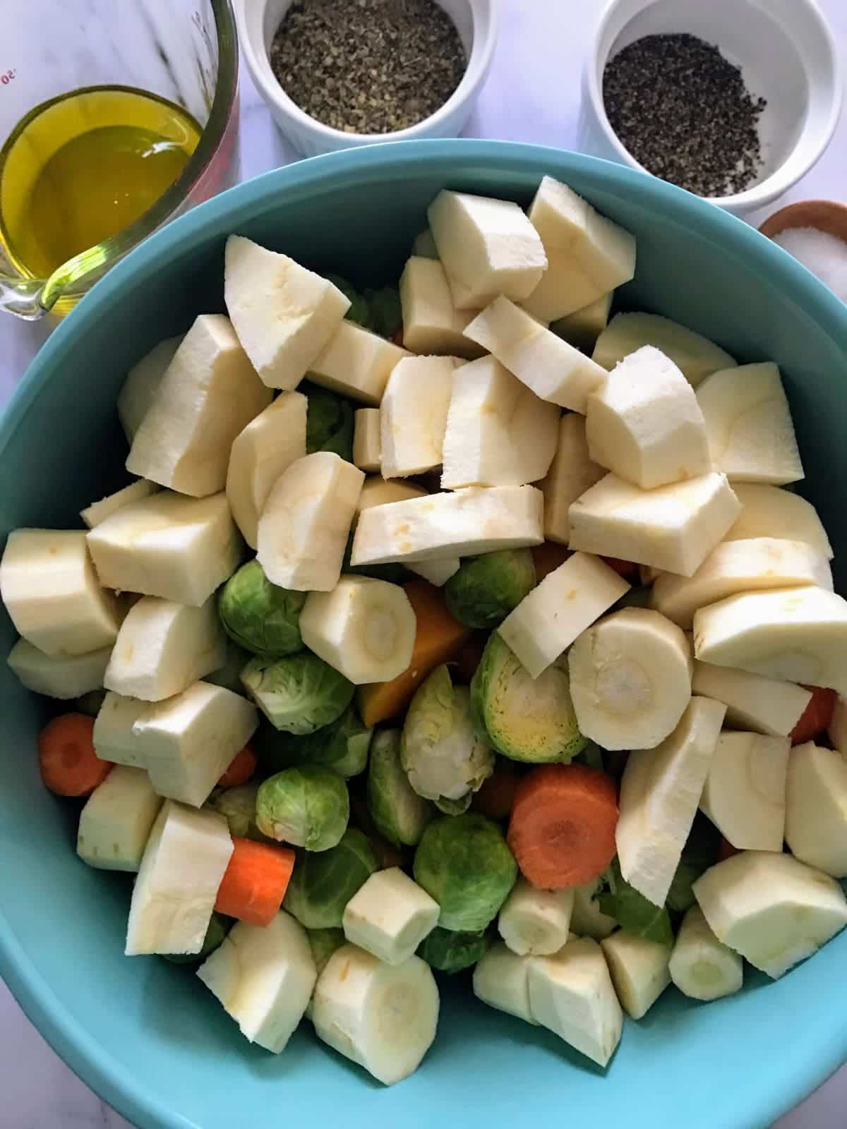 Chopped parsnips, brussels sprouts, carrots in a blue bowl to make Simple Herb-Roasted Vegetables
