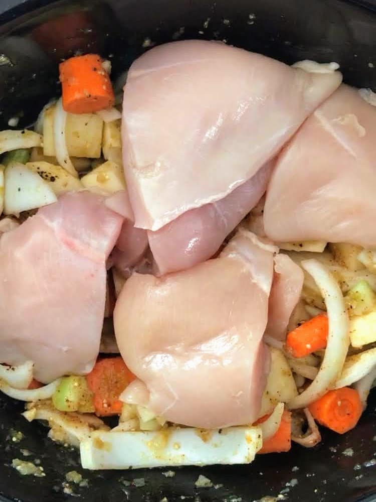 raw chicken breast on top of vegetables in slow cooker