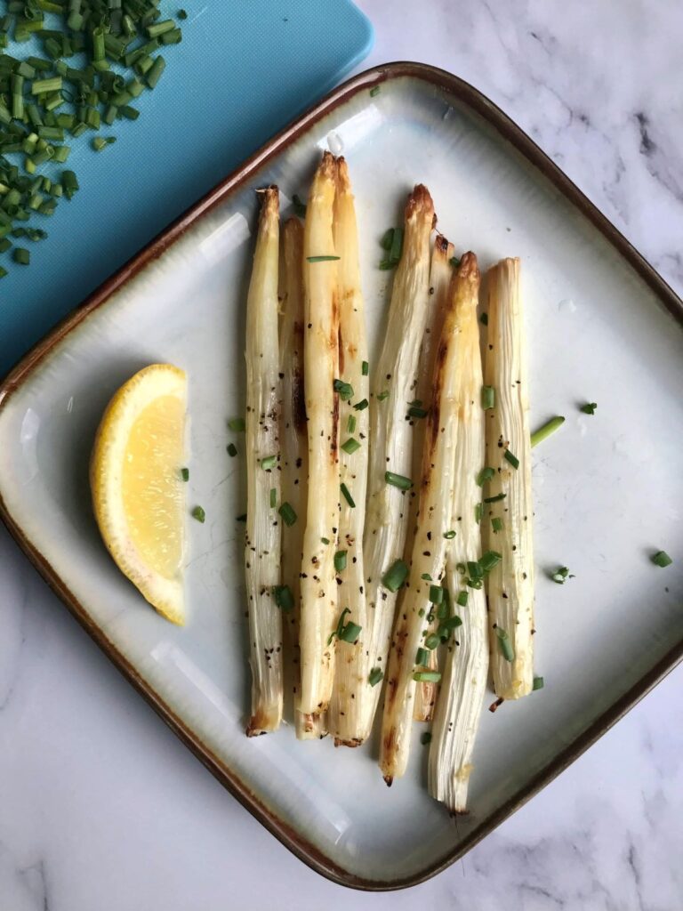 roasted white asparagus on a plate with lemon wedge