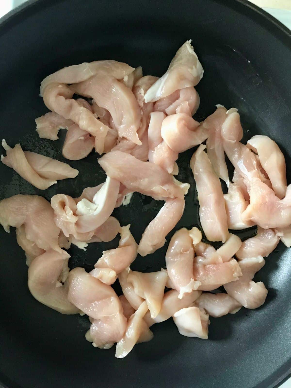 raw chopped chicken breast cooking in a skillet