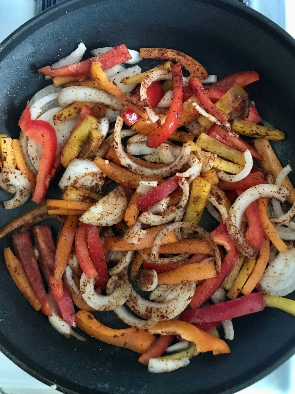 raw sliced onions and bell peppers with fajita seasoning in skillet