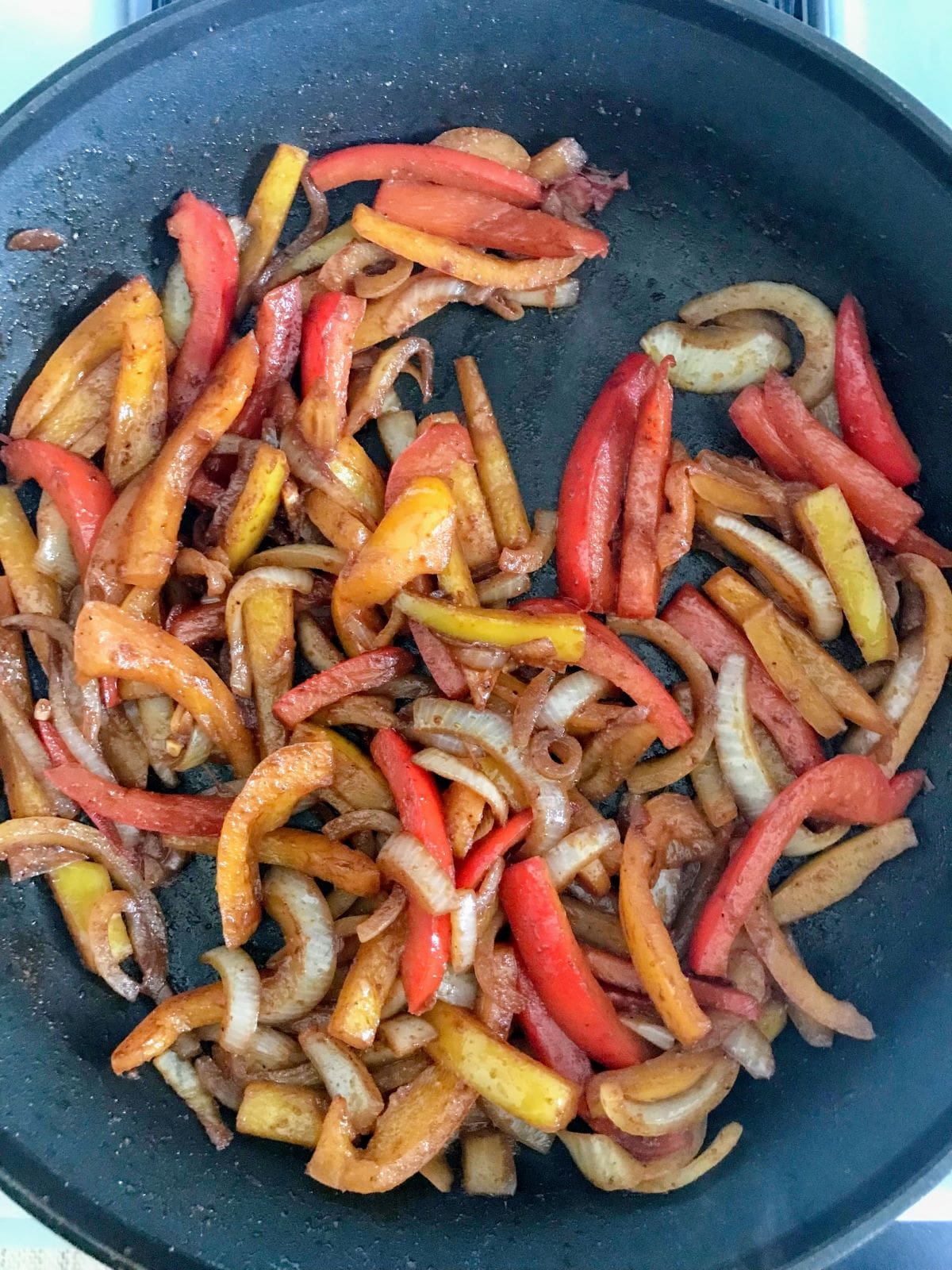sliced onions, bell peppers cooking in a skillet