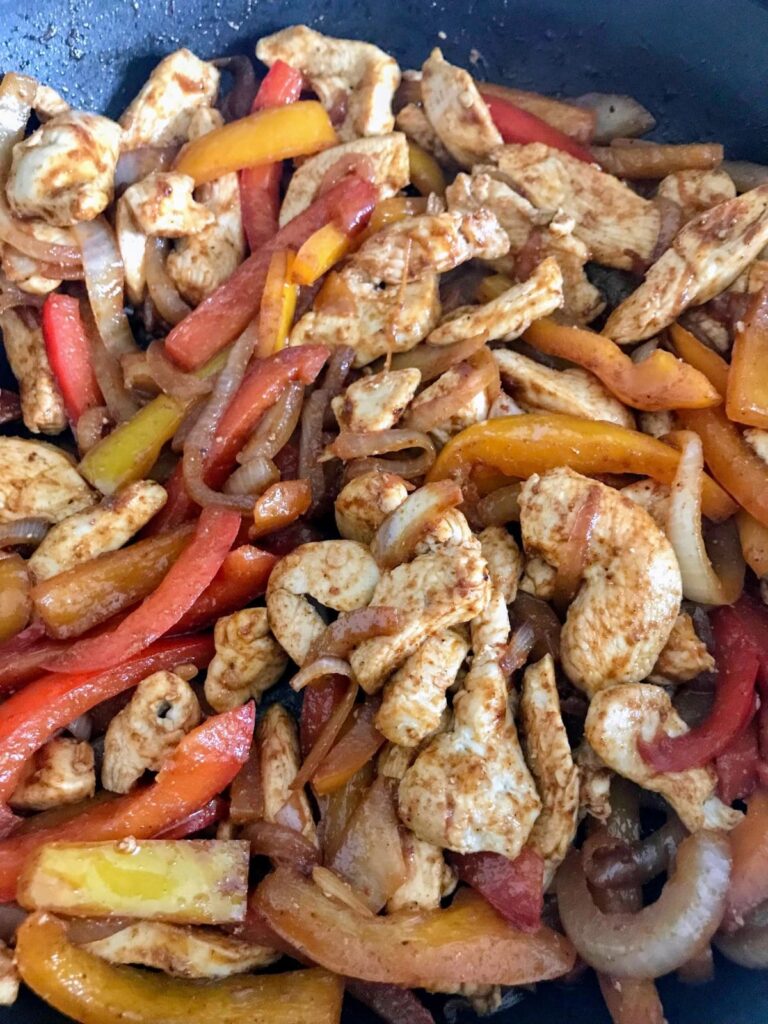 chicken, bell peppers, and onions cooking in a skillet
