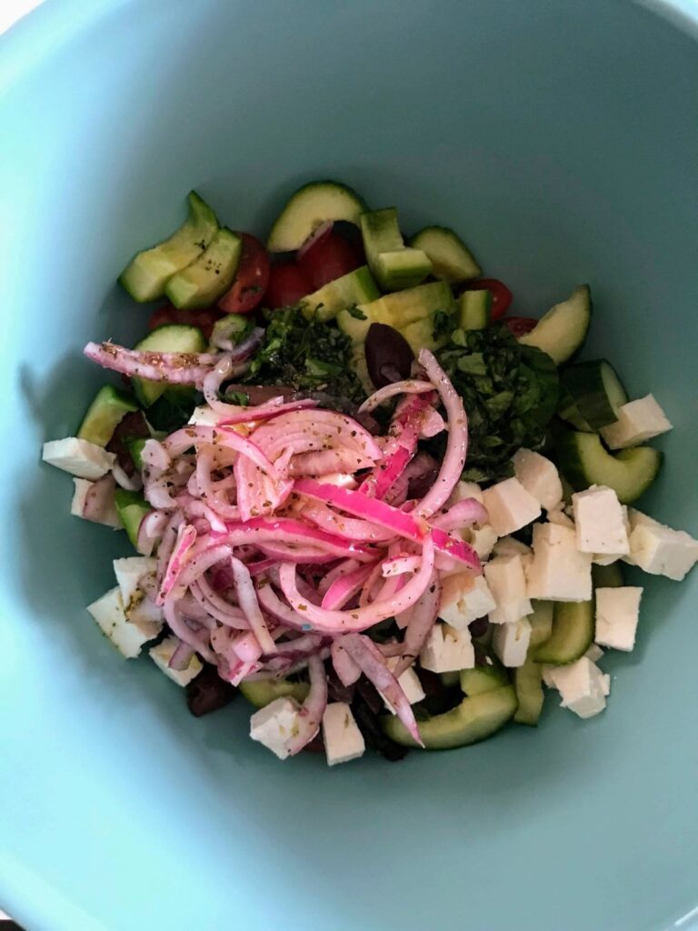 sliced red onions, fresh parsley, basil, feta cheese, and cucumbers in a bowl.