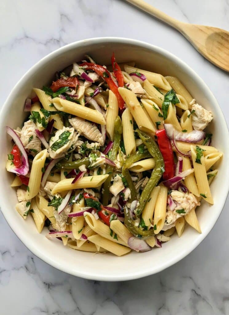 chicken bell pepper pasta salad in a white bowl and with a wooden spoon.