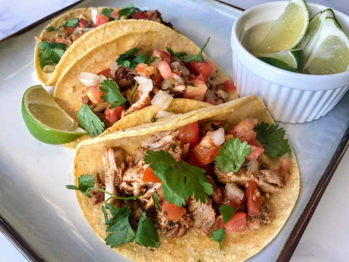 pollo asado tacos on a plate with lime wedges.