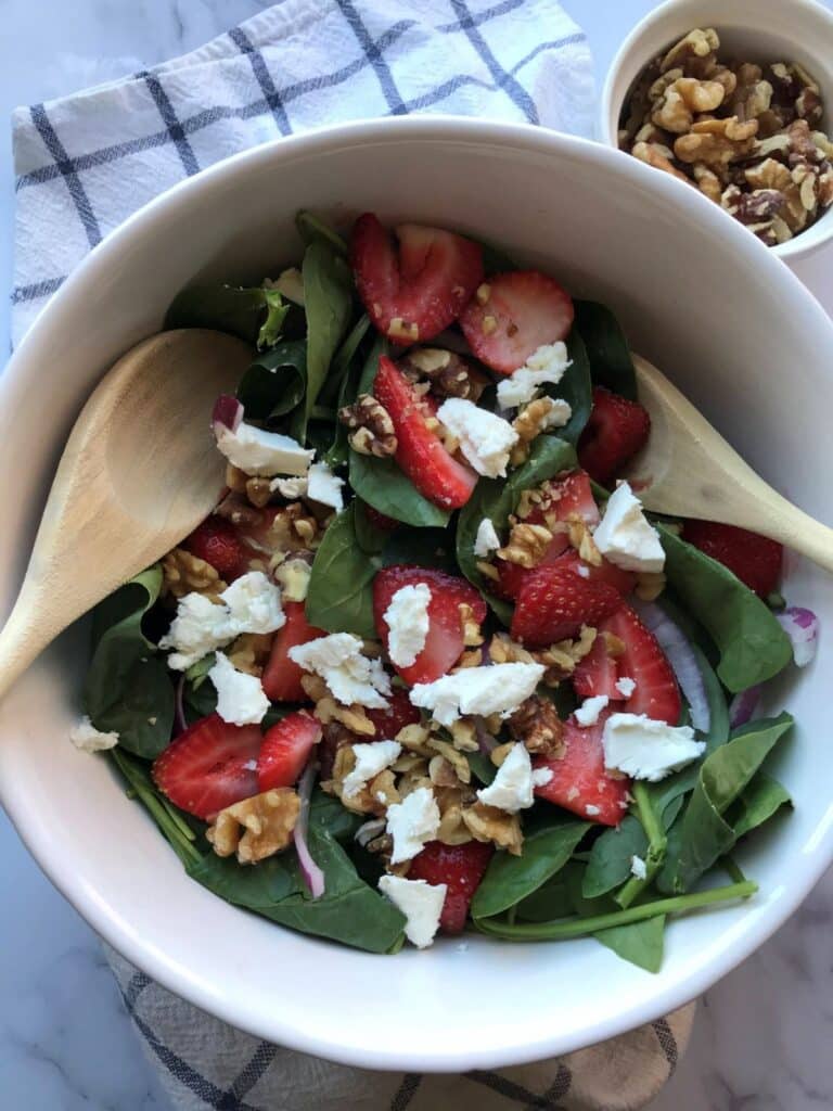 strawberry spinach salad with goat cheese and walnuts in a white bowl.