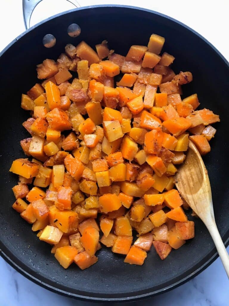 sauteed butternut squash in a skillet with a wooden spoon.