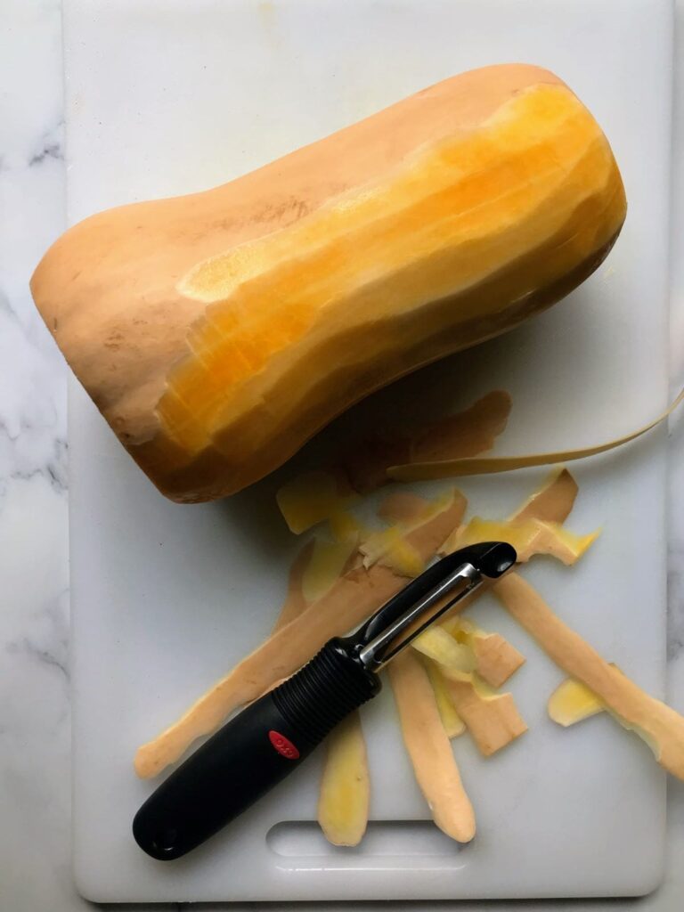 partially peeled butternut squash on a cutting board.